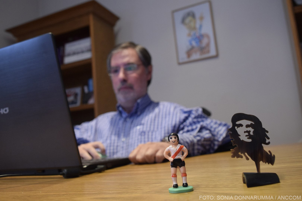 Rivas está sentado, en su oficina, frente a la computadora. Sobre el escritorio posan dos muñecos: uno de River y otro con la cara del Che Guevara.