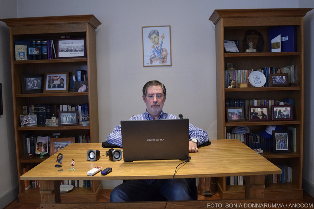 Rivas está sentado frente a la computadora en su oficina. Se lo ve de frente y, a sus espaldas, dos bibliotecas con libros y fotografías.