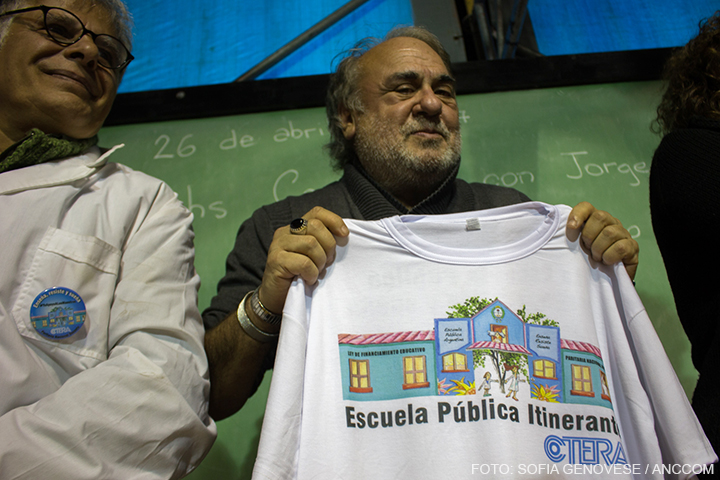Alemán sostiene una remera con una ilustración de la Escuela Pública Itinerante.