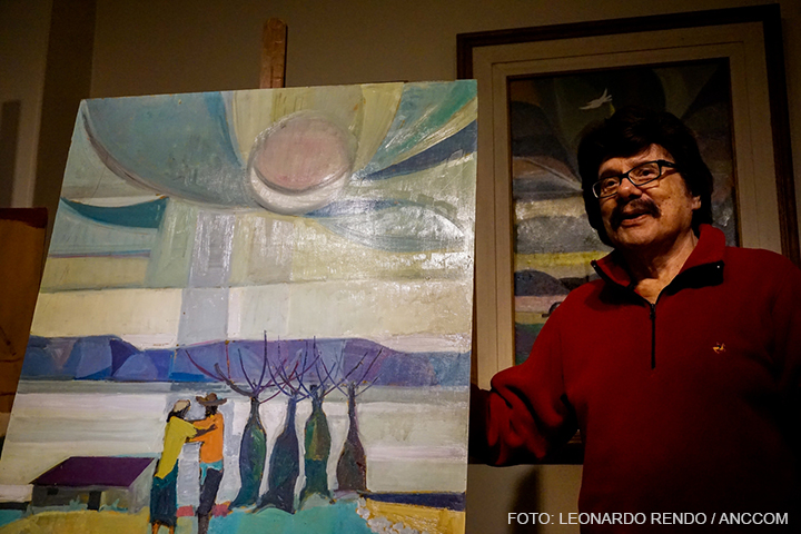 El cantante Ramón Ayala se encuentra parado de frente sosteniendo un cuadro que es una pintura de un paisaje con árboles.