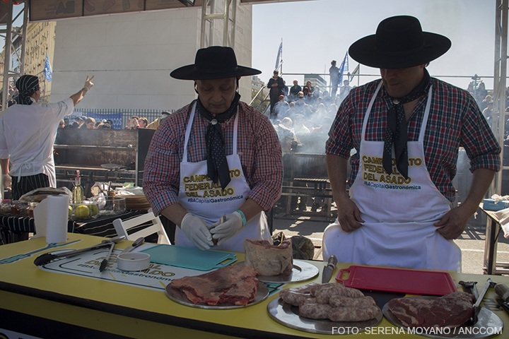 Dos parrilleros vestidos con ropas tradicionales se encuentran preparando la carne cruda.