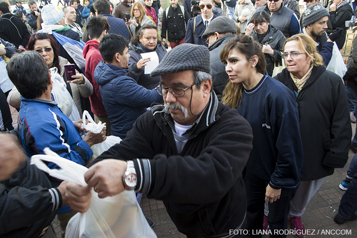 Un señor recibiendo una bolsa blanca con bananas dentro de la misma, de fondo mucha gente con bolsas de bananas en sus manos.