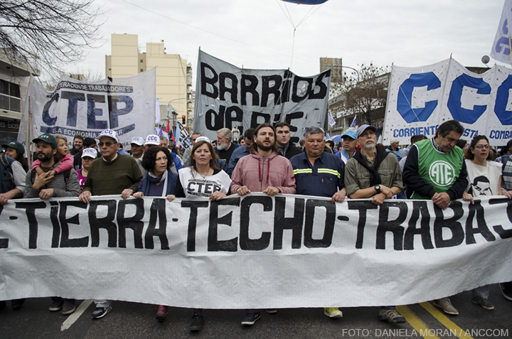 Grupo de personas marcha con una bandera al frente en la que se lee: "Tierra-Techo-Trabajo". Detr{as de ellos las banderas de las agrupaciones que convocaron la marcha.