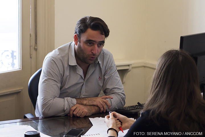 Julián Axat está sentado con los brazos apoyados en su escritorio. Se lo ve en pleno diálogo con su entrevistadora.