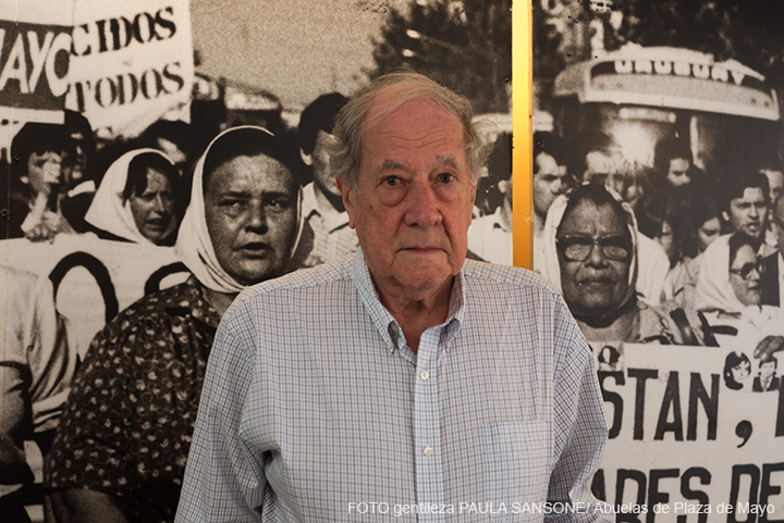 Robert Cox está de pie en el Espacio de Memoria y Derechos Humanos. Está parado en Detrás suyo hay una gigantografía que muestra a Madres de Plaza de Mayo protestando por la aparición de sus hijos.