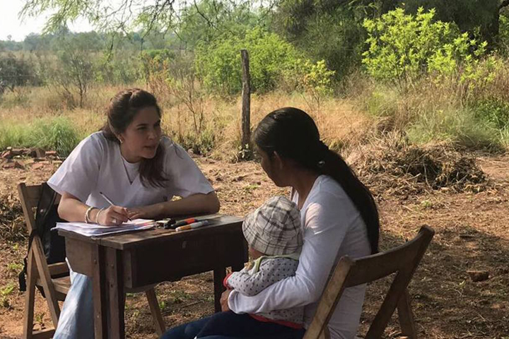 Una mujer y su bebé teniendo una consulta al aire libre con una Médica voluntaria de la Fundación Alma.