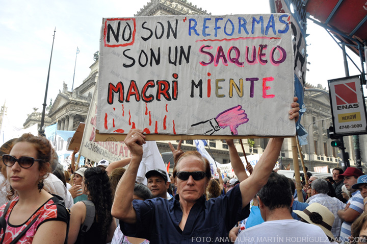 Un hombre entre los manifestantes, sosteniendo un cartel que dice: "No son 'reformas', son un saqueo. Macri miente".