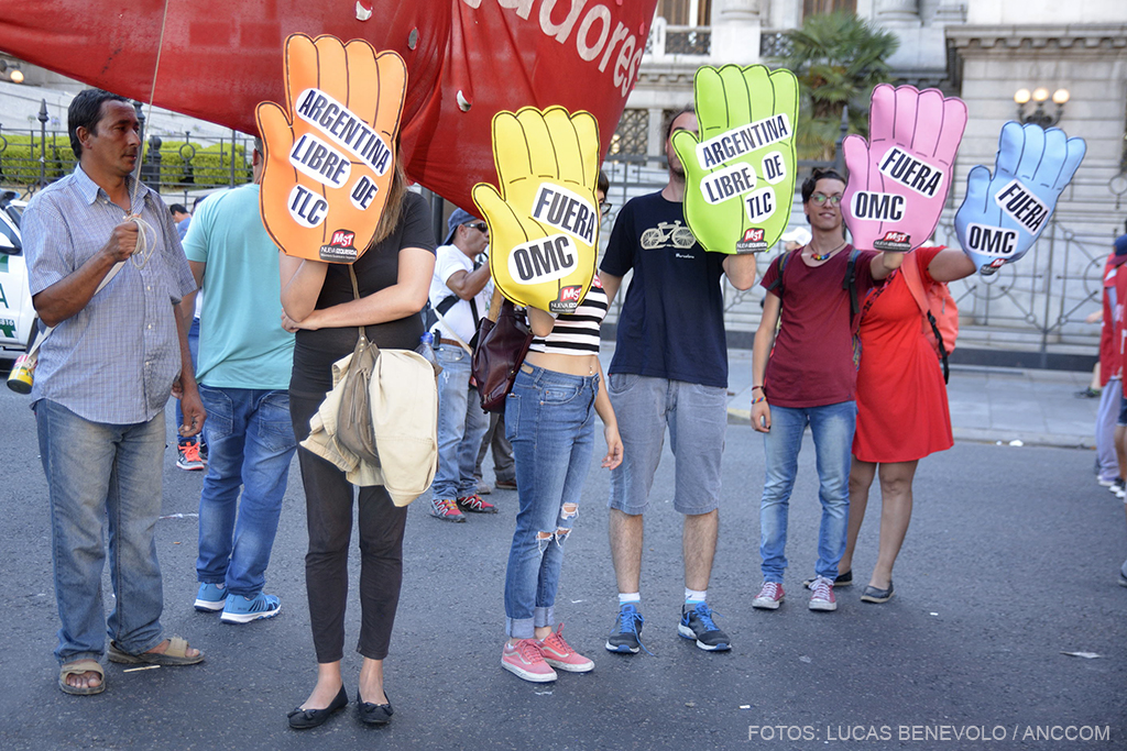 Manifestantes exhiben carteles en forma de mano donde se lee "Argentina libre de TLC" y "Fuera OMC"