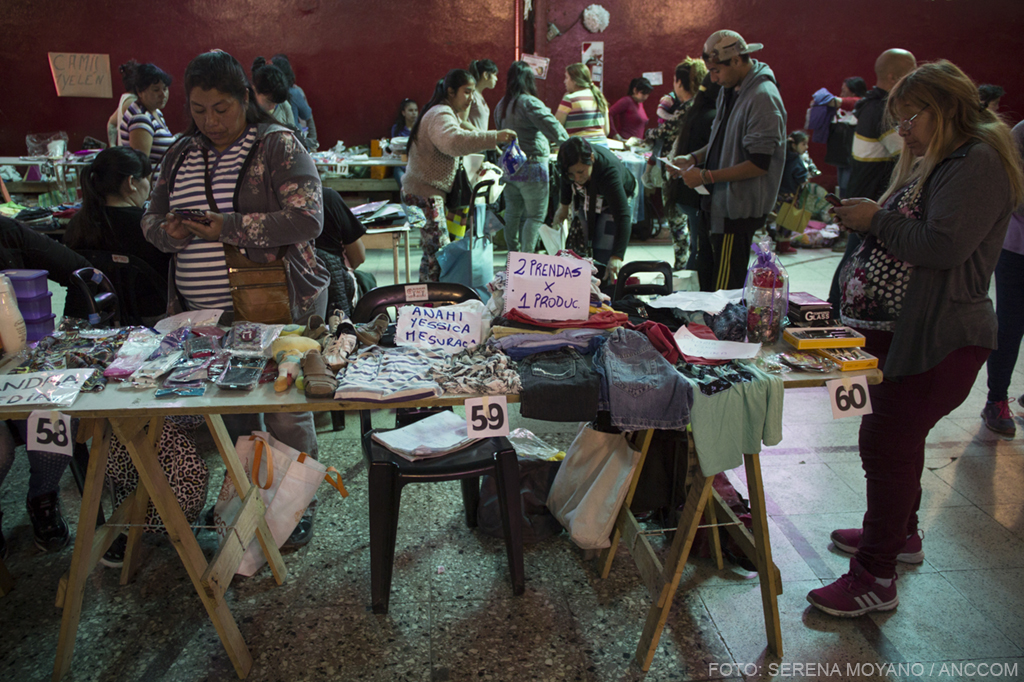 Dos mujeres venden ropa sobre mesas de madera en el club Unión de Merlo.