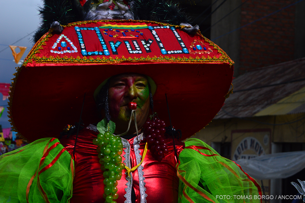 Un hombre con traje colorido lleva puesto un gran sombrero rojo que dice Oruro.