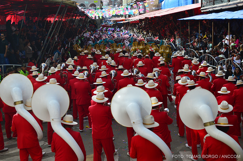Una banda de músicos, todos vestidos de rojo, tocan sus instrumentos de viento en las calles de Oruro.