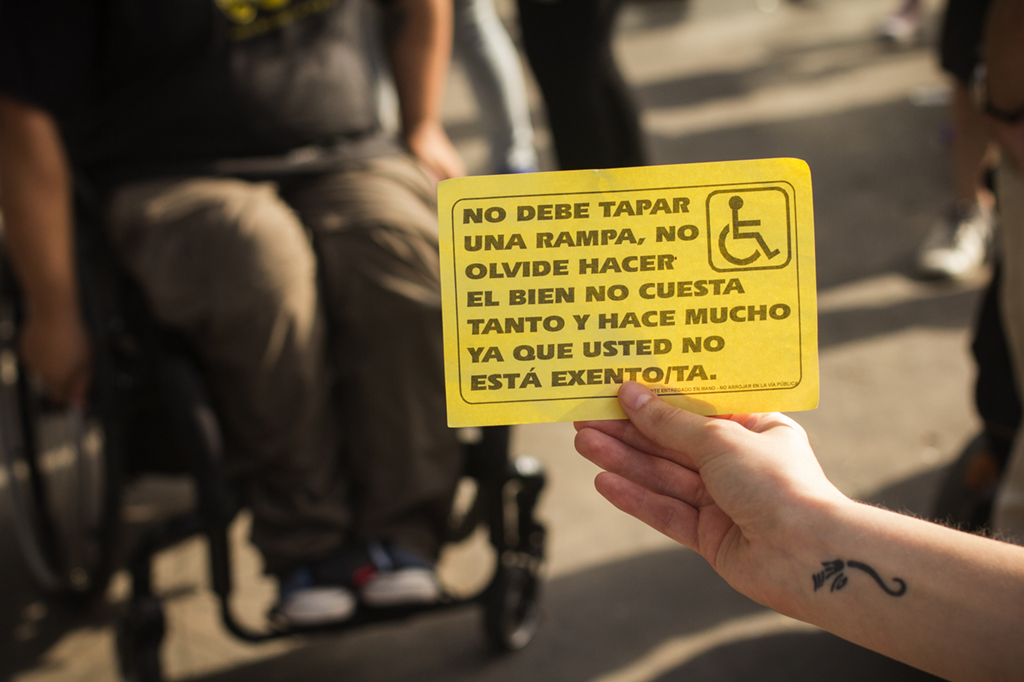 imagen de un papel amarillo que dice "No debe tapar una rampa, no olvide hacer el bien no cuesta tanto y hace mucho ya que usted no está excento/ta"