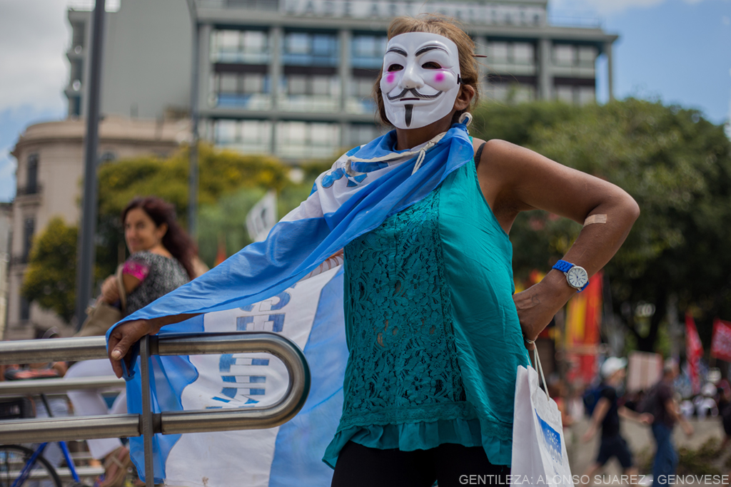 mujer tapandose el rostro con una mascara y lleva colgada como una capa la bandera argentina