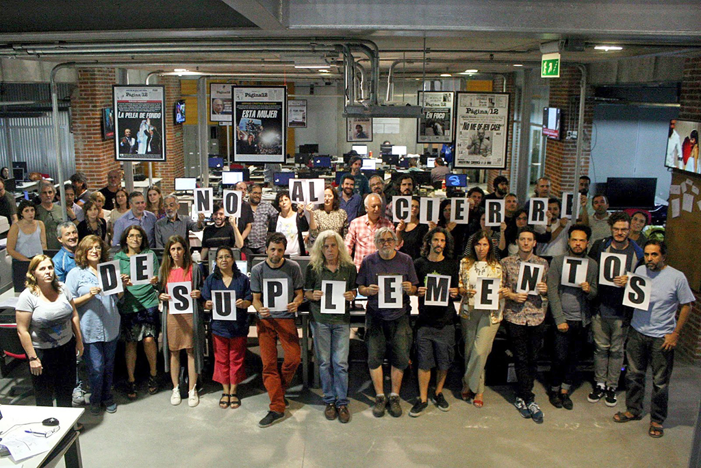 Trabajadores de Página 12 sosteniendo carteles con letras que juntos  conforman la frase "No al cierre del suplemento".