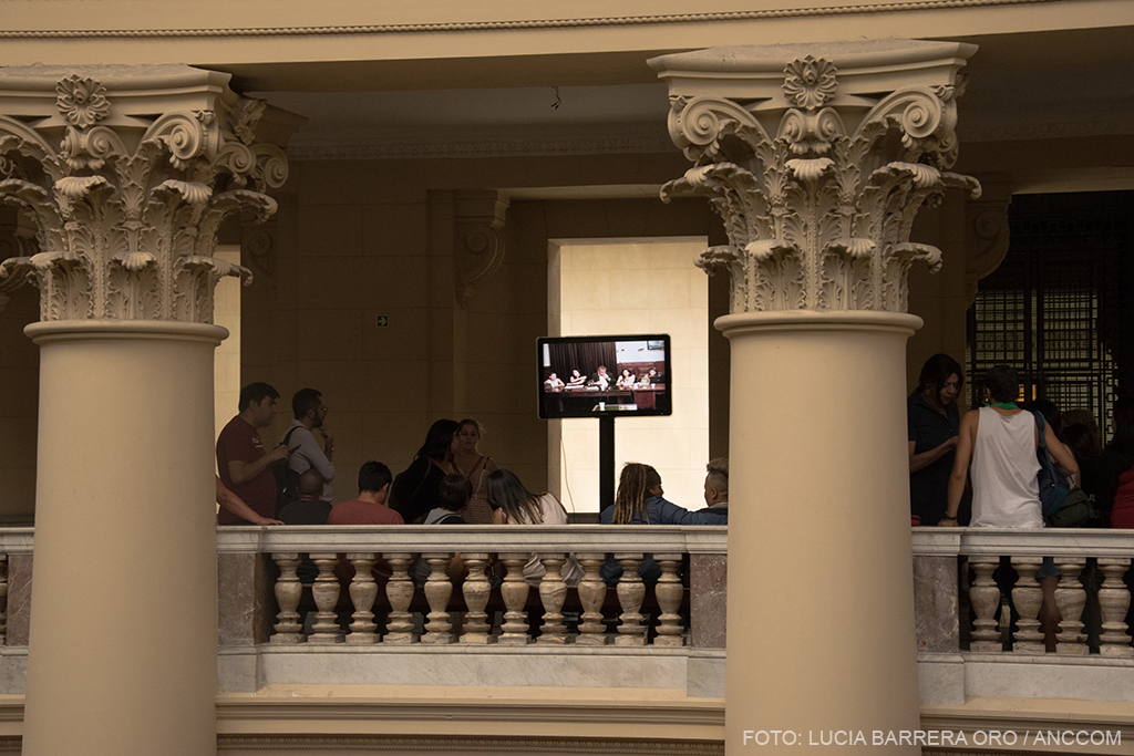 familiares y amigos en un pasillo del tribunal, viendo en una pantalla el juicio por el travesticidio de Diana.