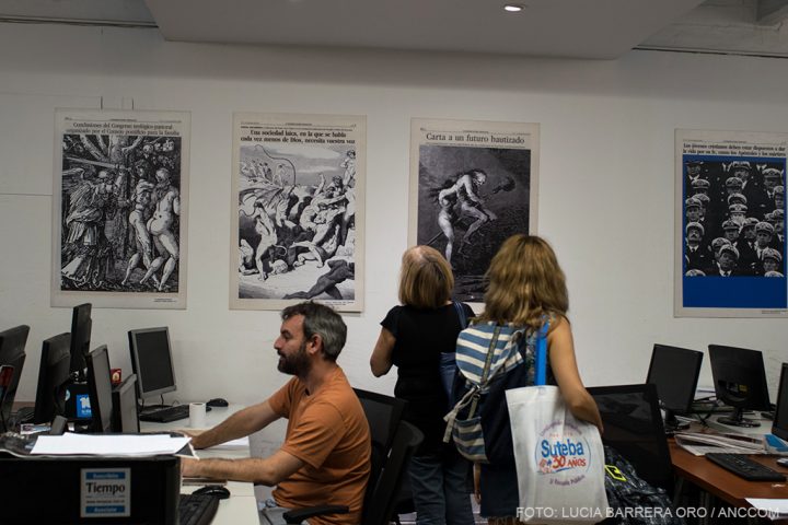 Un periodista del diario Tiempo Argentino trabajando mientras dos mujeres miran imágenes de la muestra en la pared