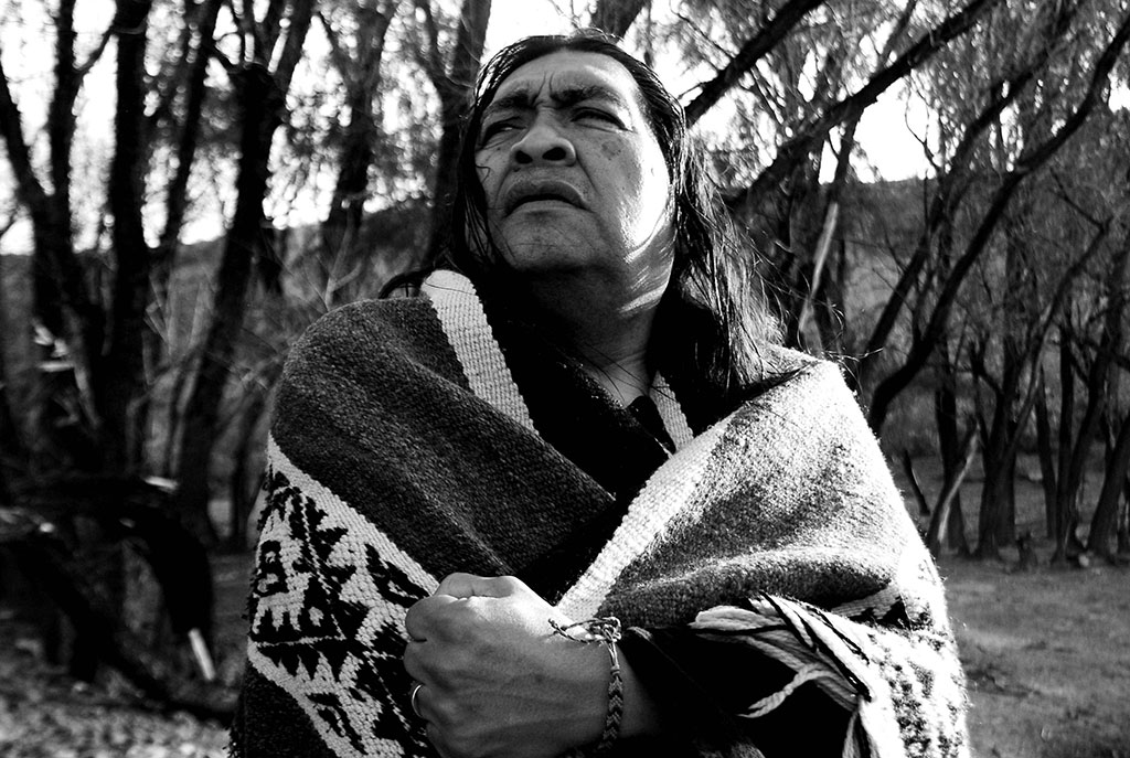 Rubén Patagonia posando vistiendo un poncho, foto en blanco y negro con fondo de árboles.
