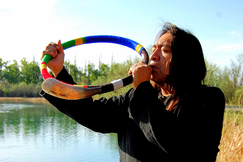 Rubén Patagonia con instrumento, foto en colores y fondo de lago.