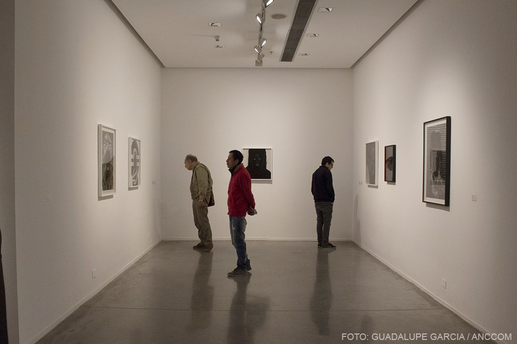 Imagen de la sala , se ven tres paredes y tres personas observando fotografías.