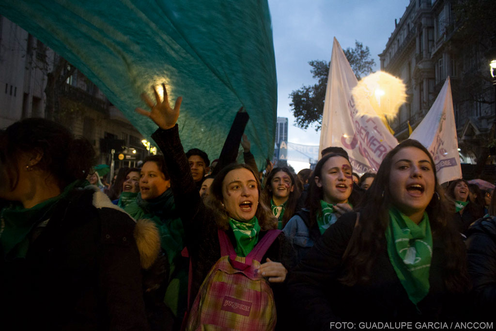 Mujeres marchando, cantado, con pañuelos y banderas verdes.