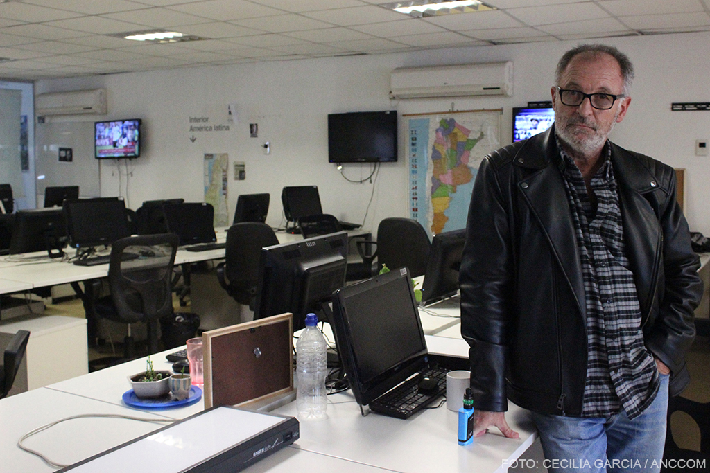 Carlos Brigo, fotógrafo, despedido de la Agencia de Noticias Telam, parado con fondo de escritorios con computadoras vacíos. 