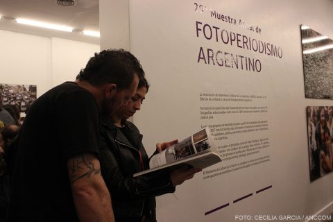 Un hombre y una mujer mirando un libro con las fotografías junto a la entrada de la exposición
