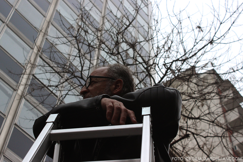 Carlos Brigo apoyado sobre una escalera en la calle. edificio de fondo, imagen tomada desde abajo.