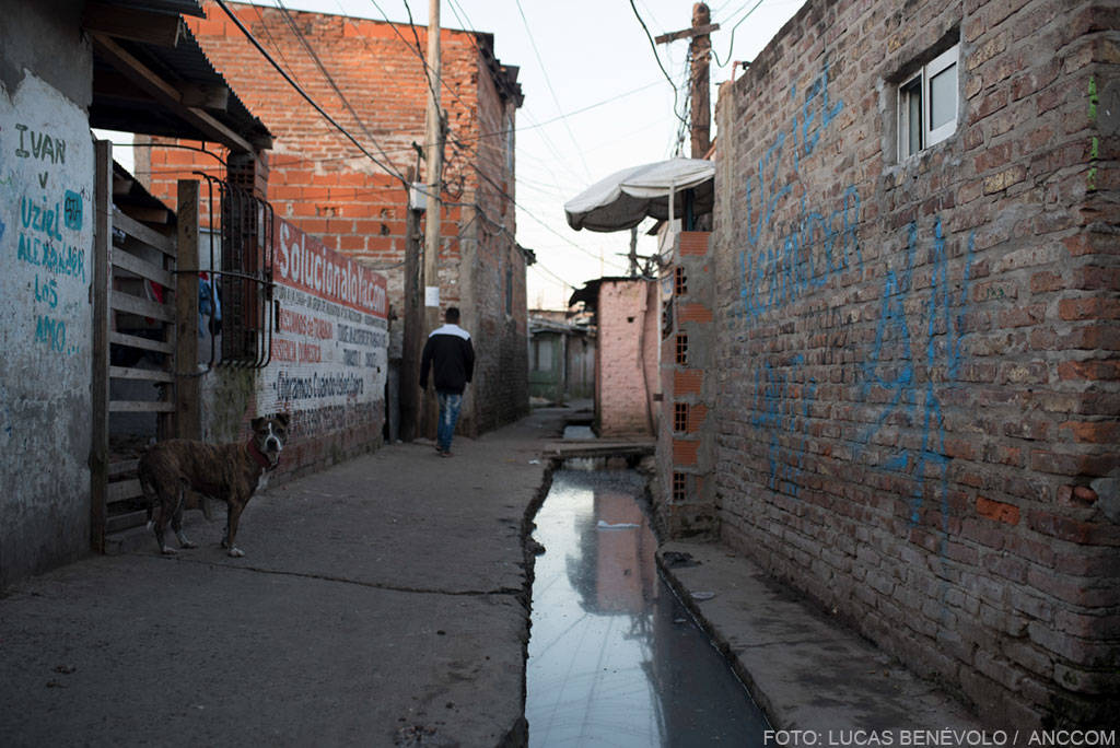 Un hombre caminando por un calle angosta, entre edificaciones precarias de ladrillos