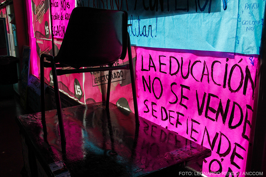 Silla sobre una mesa, delante de un afiche que reza "la educación no se vende, se defiende".