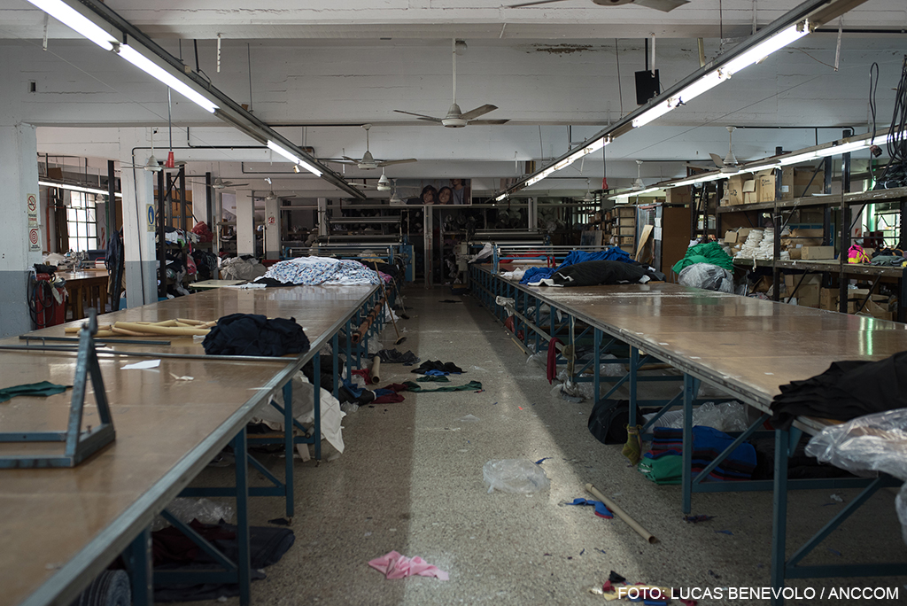 Interior de una fábrica, con mesas de trabajo vacías y trapos tirados en el piso. 