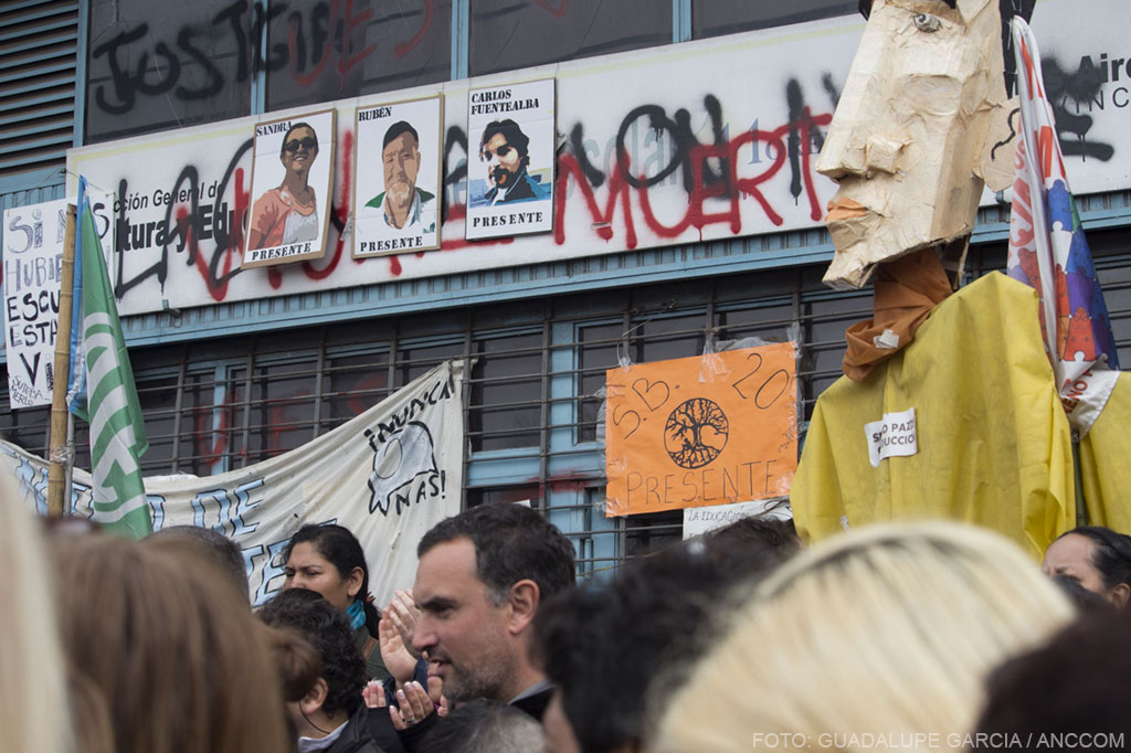 Hombres y mujeres en la movilización y detrás de ellos carteles pegados en la pared exigiendo justicia.