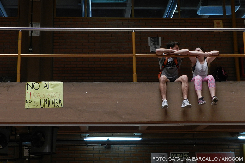 Dos jóvenes sentados en el primer piso del edificio en disputa y un cartel que dice "no al traslado, no a la UNICABA"